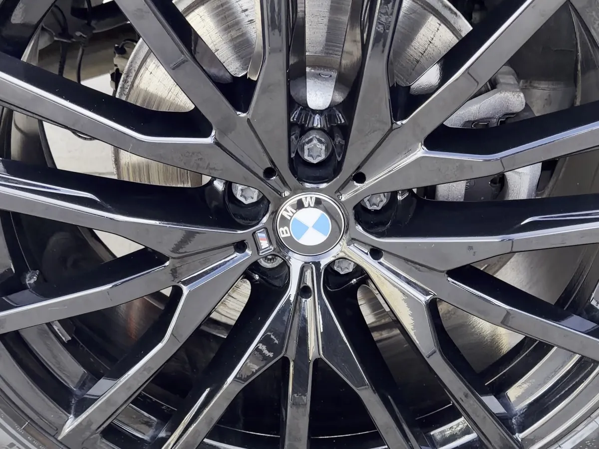 Same BMW X6 wheel after detailing — gloss black mirror finish
